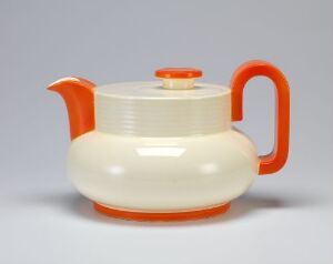  A vintage cream and orange teapot with a ribbed texture, featuring a smooth orange handle and spout, and a flat, round-lidded top with an orange knob, displayed against a soft grey background.