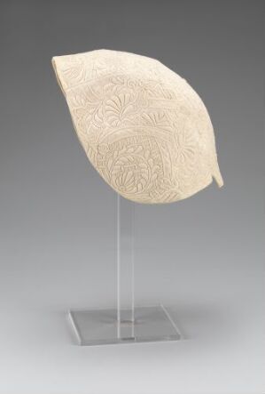  A cream-colored leaf sculpture with intricate embossed patterns displayed on a transparent vertical stand against a light gray background.