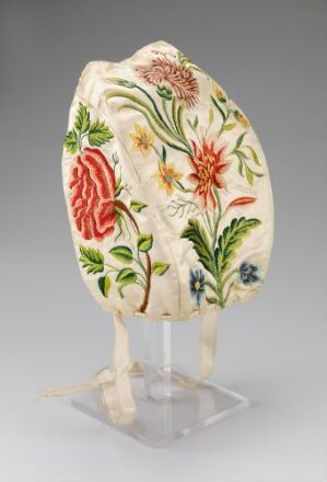  An ornate, egg-shaped object with a cream background, adorned with detailed floral patterns in orange, pinkish-red, yellow, blue, and various shades of green, displayed on a clear stand.