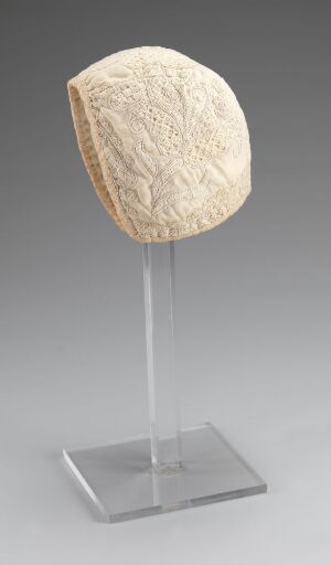 
 An irregularly shaped pale-colored object with intricate textural patterns, mounted on a clear stand against a gradient gray background.