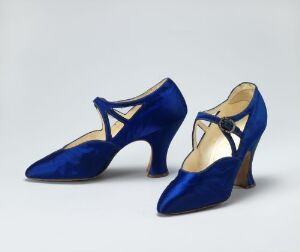  A pair of cobalt blue velvet high-heeled shoes with pointed toes and delicate strap details, displayed against a light grey background.