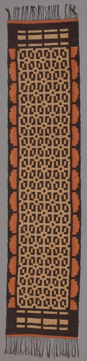  A long, vertical textile with a soft grey background, featuring symmetrical borders of terracotta circular motifs and black and tan geometric shapes, surrounding a central pattern of blocks with concentric circles in earth tones.