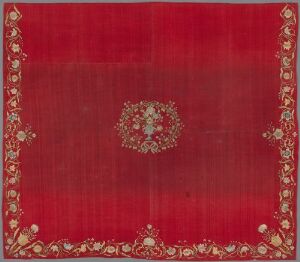  A square-shaped textile with a deep red background, bordered by golden floral patterns and a central circular golden medallion, indicating a luxurious and ornate fabric, possibly of historical significance.