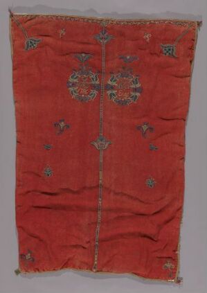  An antique textile with a dark red background featuring intricate symmetrical embroidery in blue, cream, green, and gold. The fabric shows signs of wear, and the detailed patterns suggest a historical or cultural significance. Artist name and title are unknown.