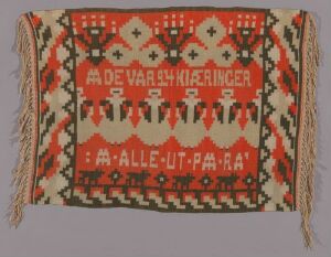  A handwoven textile by artist Sigrun Munthe, featuring a red background with off-white and black geometric patterns, stylized figures, and text. The intricate design is framed by black and white fringes at the top and bottom.