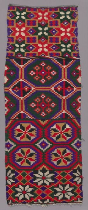  A vertical textile with a detailed geometric pattern, featuring a color palette of purple, red, green, blue, and white, with repeating diamond shapes and intricate motifs.