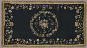  An ornate rug with a dark navy blue or black background featuring a symmetrical floral design with a central medallion. The rug displays intricate patterns in shades of gold, cream, greens, pinks, light blues, and yellows framed by a series of decorative borders.