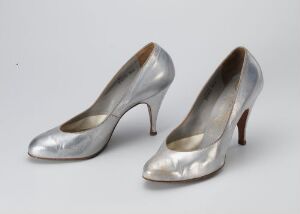 
 A pair of elegant metallic silver high-heeled shoes with a rounded toe, displayed against a light grey background.