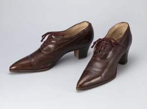  A pair of polished brown leather men's dress shoes with pointed toes and round dark brown laces, set against a plain grey background.