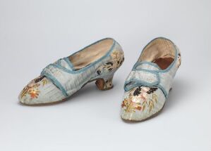  Antique women's shoes with light blue fabric and floral pattern, adorned with blue bows, set against a light grey background.