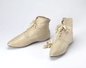  A pair of vintage beige lace-up ankle shoes with pointed toes displayed against a neutral grey background, reflecting historical craftsmanship and fashion. Artistname and title are unknown.