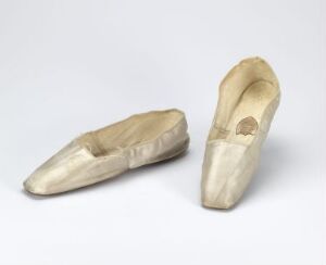  A pair of well-worn beige ballet shoes on a light grey background.