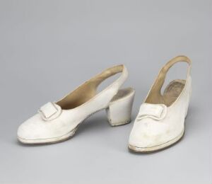  A pair of vintage off-white women's shoes with square heels and small white buckles, set against a neutral gray background. The material of the shoes appears to be a type of aged leather.