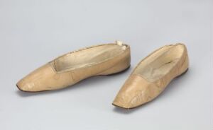 
 A pair of wooden medieval-style pointed shoes, referred to as "poulaines," displayed on a pale gray background. The shoes are light wood in color, with visible grain patterns and a polished surface.