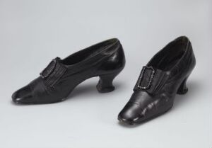  A pair of vintage black women's shoes with pointed toes and decorative buckles on a light grey background. Artist name and title are unknown.