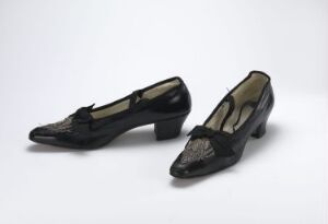  A pair of elegant black leather women's shoes with a low heel and a decorative design on a pointed toe cap, presented against a light grey background.