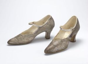  A pair of vintage greyish-taupe women's shoes with a low heel and a subtle floral pattern against a neutral background. The shoes have a slightly pointed toe and cream-colored insoles, indicative of early to mid-20th-century fashion.