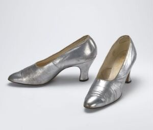  A pair of silver-gray metallic high-heeled shoes with pointed toes, displayed against a neutral background. The shoes exhibit a polished, brushed appearance and feature modest heels, suggesting a refined and versatile design.