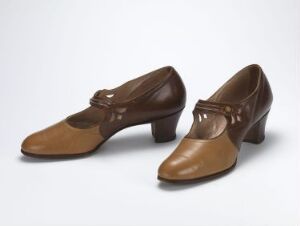  A pair of vintage women's shoes in a two-tone brown color scheme with a T-bar strap featuring a small buckle on a light background.