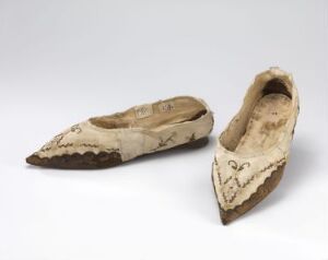  A pair of historical beige and brown embroidered women's pointed shoes showing signs of wear against a light gray background.