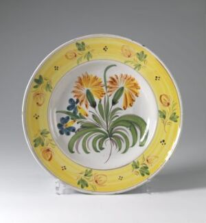  A vibrantly painted ceramic plate with a yellow rim and a central hand-painted floral design featuring orange flowers, blueberries, and lush green leaves, displayed on a clear stand against a light grey background. Artist name and title are unknown.