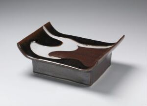 
 A porcelain object titled "Fat" by Anne Marie Backer Mohr, featuring an abstract design with raised edges and a contrasting color scheme of glossy white and matte dark brown glazes.