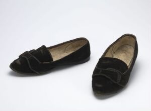  A pair of elegant black velvet women's flat shoes with horizontal strap details on the vamps, placed neatly on a light to medium grey background.