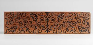  A horizontal decorative panel with a warm terra-cotta background featuring a detailed, symmetrical pattern of intertwined floral and foliate motifs in a darker shade, reminiscent of traditional carved or molded decorative art.