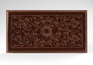 Alt-Text: Intricately carved wooden panel with symmetrical patterns and a central circular motif, in rich brown tones against a neutral background. Artist's name and title are unknown.