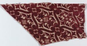  A patterned textile fragment featuring an ornate burgundy and off-white scroll design, with geometric motifs interlaced throughout, against an irregularly shaped backdrop.