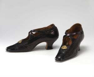  A pair of polished black vintage T-strap women's shoes with moderate heels, displayed against a neutral light grey background.