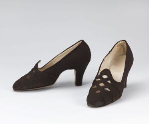  A pair of vintage dark brown women's high-heeled shoes with decorative cutouts and a light beige interior, set against an off-white background.