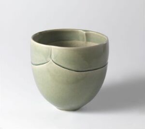  A pale green ceramic bowl with a segmented design that resembles four overlapping petals, against a neutral background, showcasing its simple elegance and unique structure.