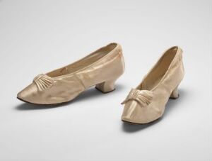  A pair of vintage beige satin women's dress shoes with modest heels and bow details, set against a light grey background.