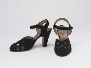  A pair of elegant black patent leather high-heeled shoes with thin straps over the toes and around the ankles, against a light gray background.