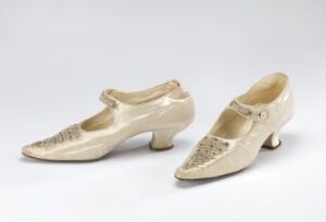  A pair of vintage ivory-colored women's shoes with pointed toes and decorative lace on the toe caps, set against a light gray background.