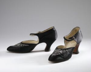  A vintage pair of black women's shoes with moderate heels and a floral-inspired perforation pattern on the toe caps against a light grey background.