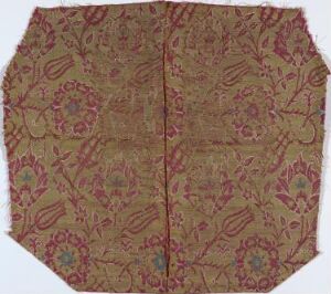  A piece of golden-tan fabric with a symmetrical floral pattern in shades of dark tan, pinkish-purple, muted blue, bright pink, and soft green, possibly a historical or ceremonial textile.