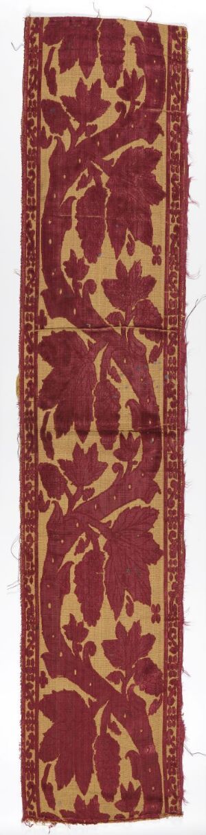  A narrow, vertical piece of fabric with a repeating pattern of golden-yellow floral motifs on a deep burgundy background, suggestive of a traditional carpet or ornate bookmark design.