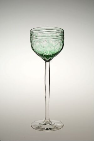  A delicate wine glass with a faint green tint in the bowl stands against a light gray background, exuding simplicity and elegance.