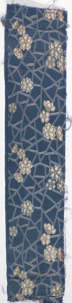  A vertical, antique-looking textile fragment with a deep blue background featuring a golden-yellow floral motif set within a lighter blue lattice pattern, showing signs of vintage wear and artistic craftsmanship.