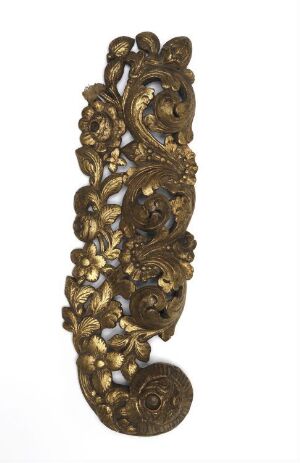  An antique-style, elongated bronze or brass decorative object, possibly a door handle, with an intricate symmetrical design featuring floral motifs and a central figure, set against a plain light background.