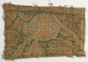 
 An antique textile fragment with an intricate plant-like design, showcasing earthy tones of browns and greens, and exhibiting significant signs of age with frayed edges and loose threads.