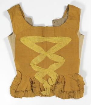  A faded mustard yellow, sleeveless historical garment with a lighter yellow-cream, intertwined spiral design on the front. The bottom edge features ruffled pleats, and there are visible signs of wear and repair.