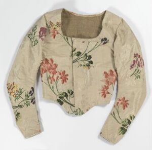  A vintage cream-colored long-sleeve bodice with floral embroidery in shades of pink, green, blue, and yellow, displayed on a neutral background, indicating historical value. Artistname and title are unknown.