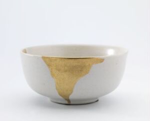  A ceramic bowl with a rough patch of ochre color inside, against a light grey background, exemplifying a simple yet striking contrast between the smooth white glaze and the textured repair. The artist name and title of the artwork are unknown.