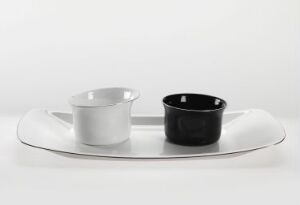  An oval silver tray on a light grey background holding a matte white cup on the left and a glossy black cup on the right.