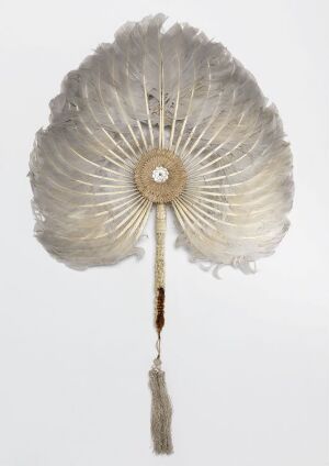  A historical circular handheld fan made of off-white feathers with a central iridescent disc and a tassel hanging from the handle against a white background.