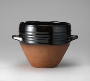  A two-toned ceramic bowl with a glossy black glazed top half, featuring horizontal ridges, and a matte terracotta bottom half, equipped with two small black glazed handles, set against a light-grey background.