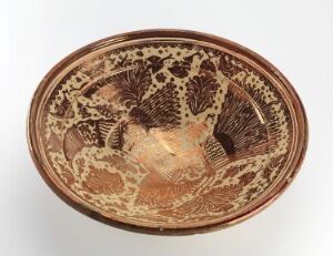  An oval-shaped terra cotta ceramic dish featuring a dark brown to black classical design of a central human figure surrounded by intricate foliage and patterned motifs, with a decorative rim. Artist and title are unknown.